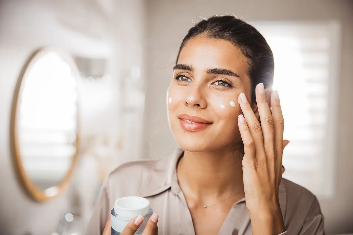 Woman applying facial cream in bathroom