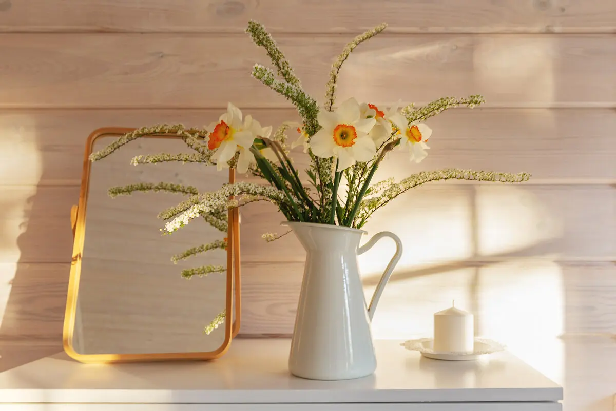 Flowers in jug with candle and mirror.